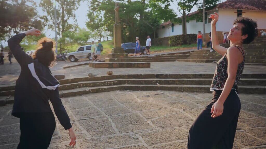 Cata and Carmen dancing outdoors in a public square, with stone steps and a cross in the background.