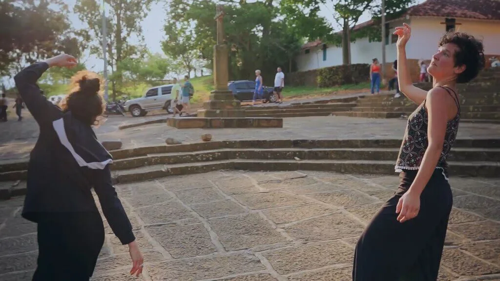 Cata and Carmen dancing outdoors in a public square, with stone steps and a cross in the background.