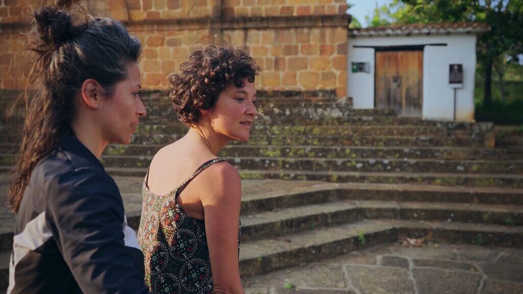 Cata and Carmen stand before a brick building, possibly a church, with stone steps.