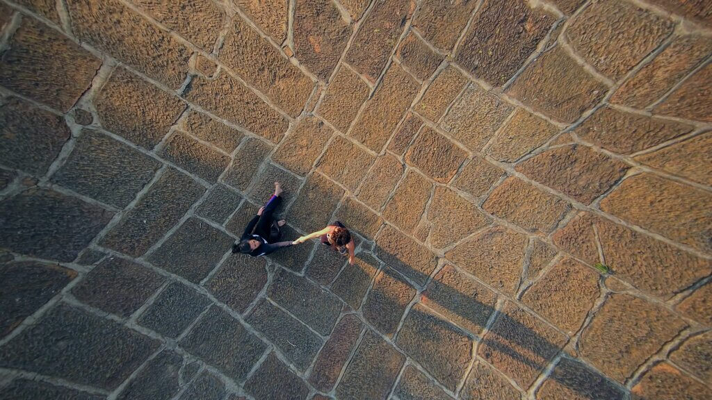 Aerial view of Cata and Carmen holding hands on a stone-paved surface.