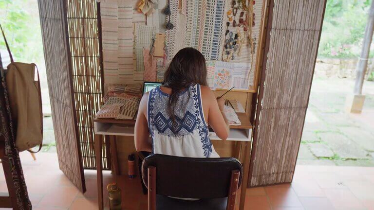 Woman crafting textiles at a desk with fabric samples, Zuahaza design inspiration.