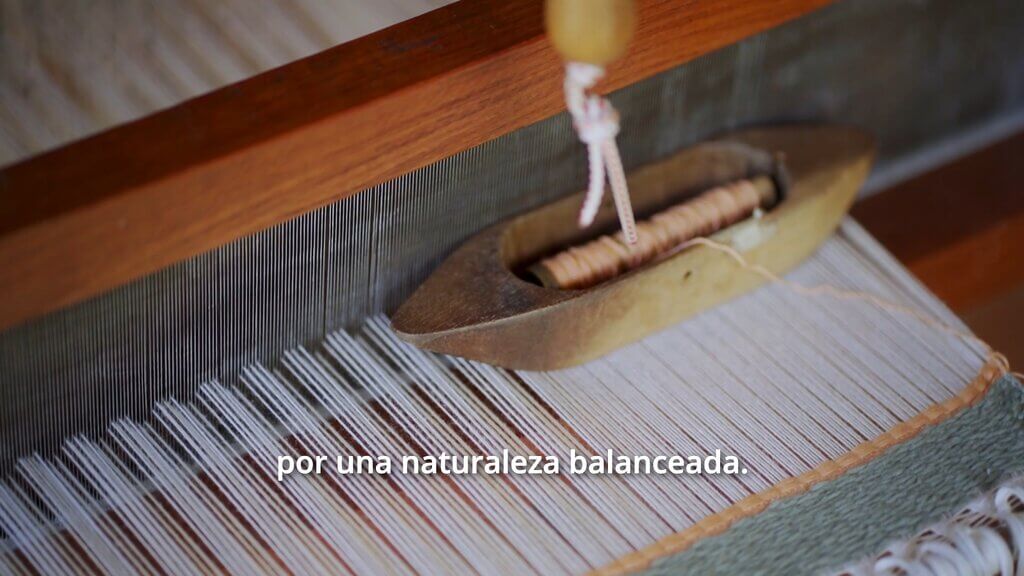 Handloom weaving with shuttle, caption reads "por una naturaleza balanceada.