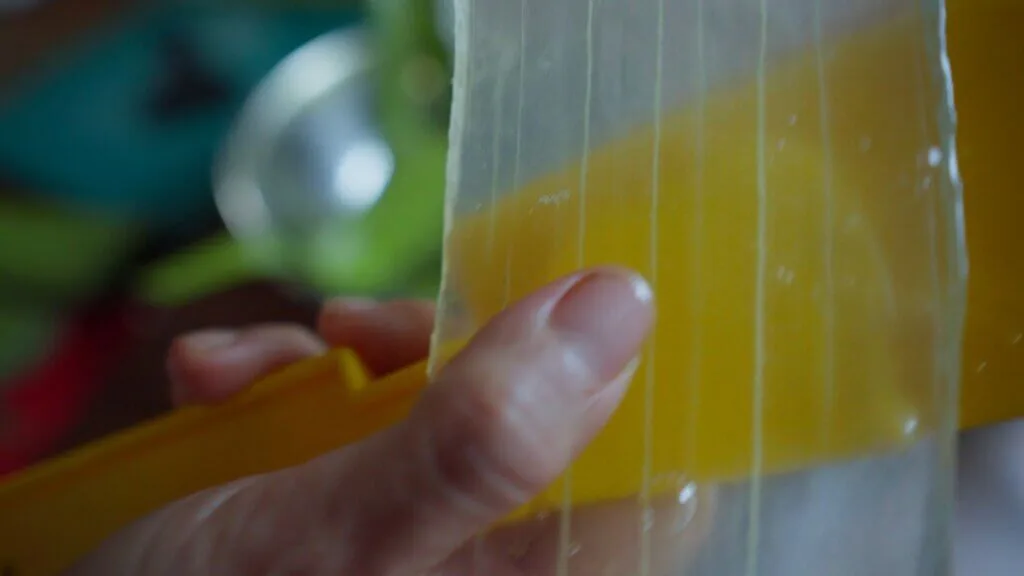 Hand holding a yellow toy xylophone with visible strings, close-up detail.