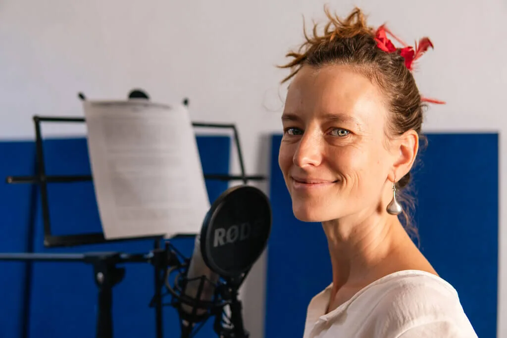 Woman recording voiceover at microphone with script. Studio setting.