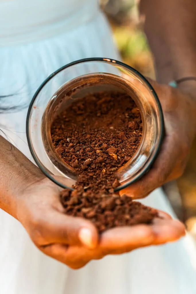 Hands pouring rich, red soil from a glass jar. Nodomondo gardening content.
