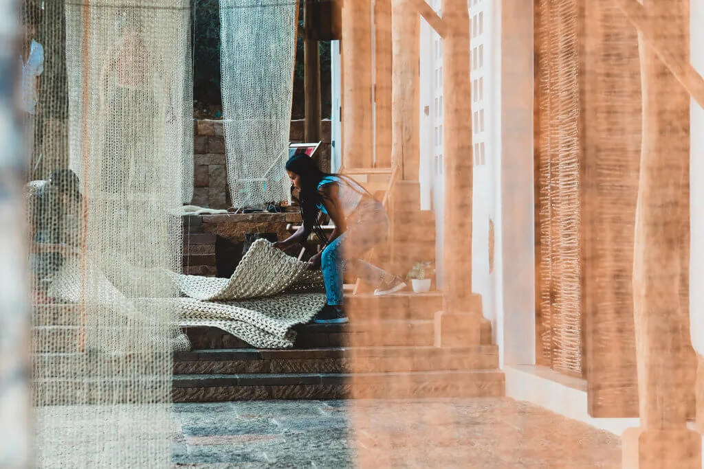 Woman arranges woven mats on stairs, possibly for Nodomondo home decor.