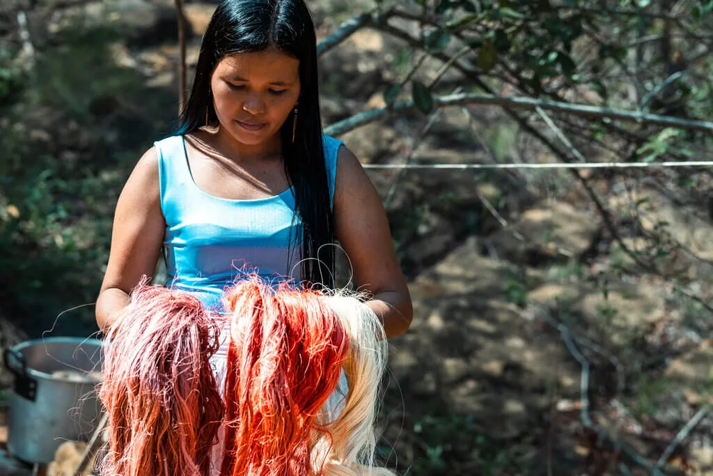 Indigenous woman holding colorful natural fibers, possibly for Nodomondo crafts or textiles.