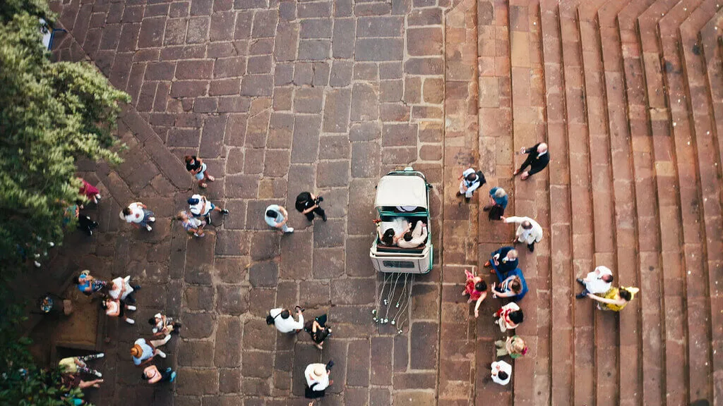 Overhead view of a wedding with a bride and groom in a carriage surrounded by guests.