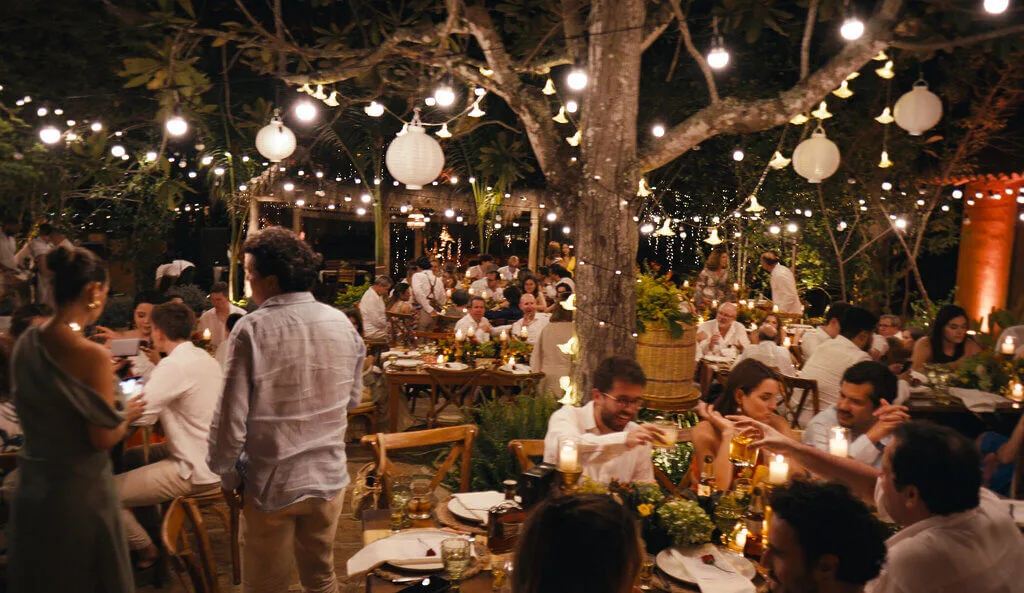 Mariana & Alex wedding reception under string lights. Guests at tables, outdoor venue.