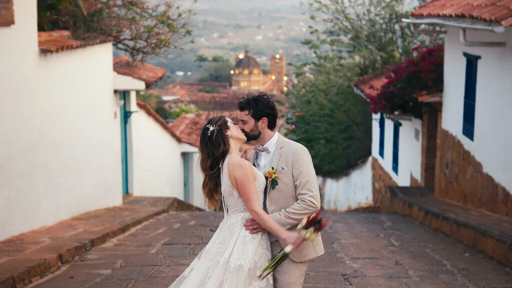 Bride and groom kiss on cobblestone street in a scenic wedding location.