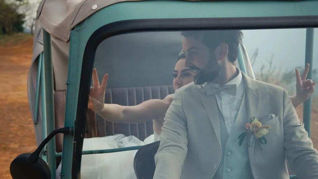 Newlyweds in a turquoise vehicle, bride making a peace sign. Wedding day joy!