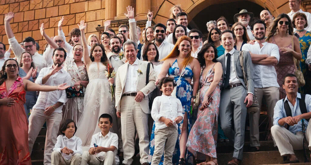 Wedding group photo of Mariana & Alex with family and friends on brick steps, celebrating their special day.