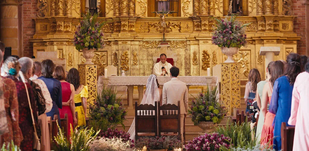 Mariana & Alex wedding ceremony in a ornate church with gold altar and floral decorations.