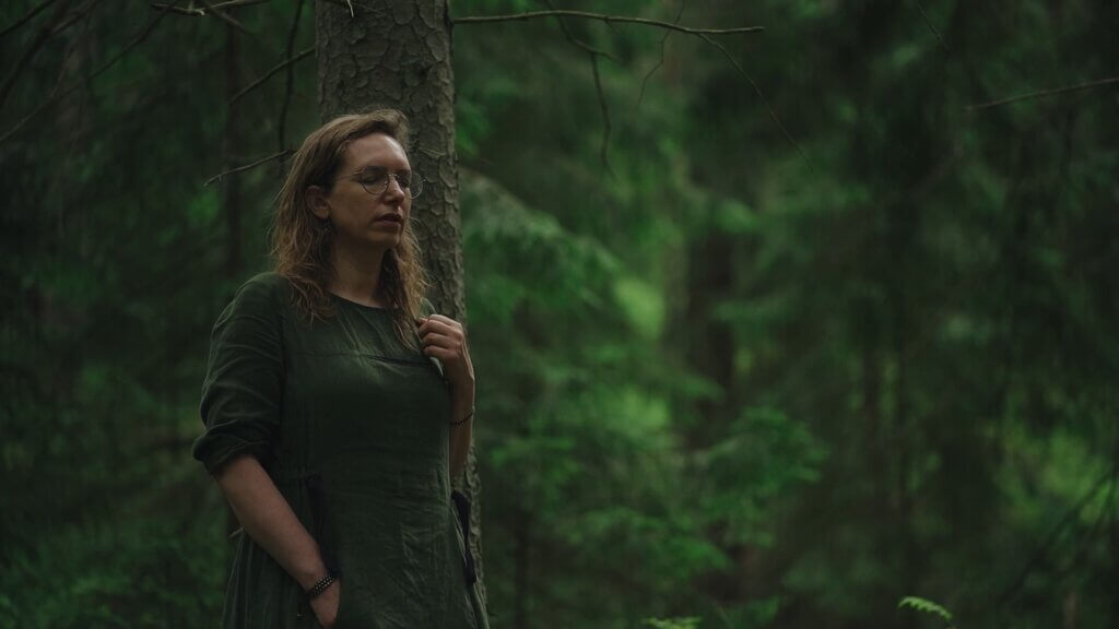 Woman in green dress stands by tree in forest. Shinrinyoku concept.