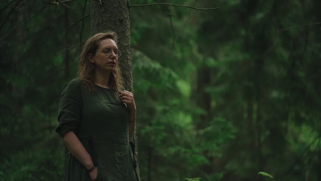 Woman in green dress stands by tree in forest. Shinrinyoku concept.