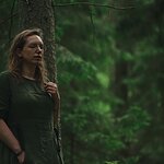 Woman in green dress stands by tree in forest. Shinrinyoku concept.