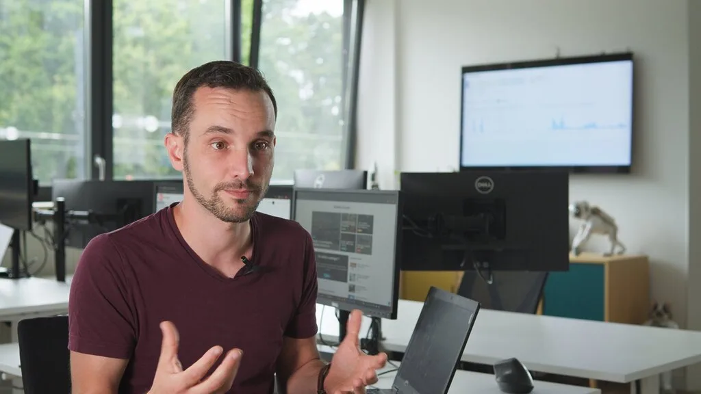 Man in office setting with multiple monitors displaying data, likely discussing Sindup analytics.
