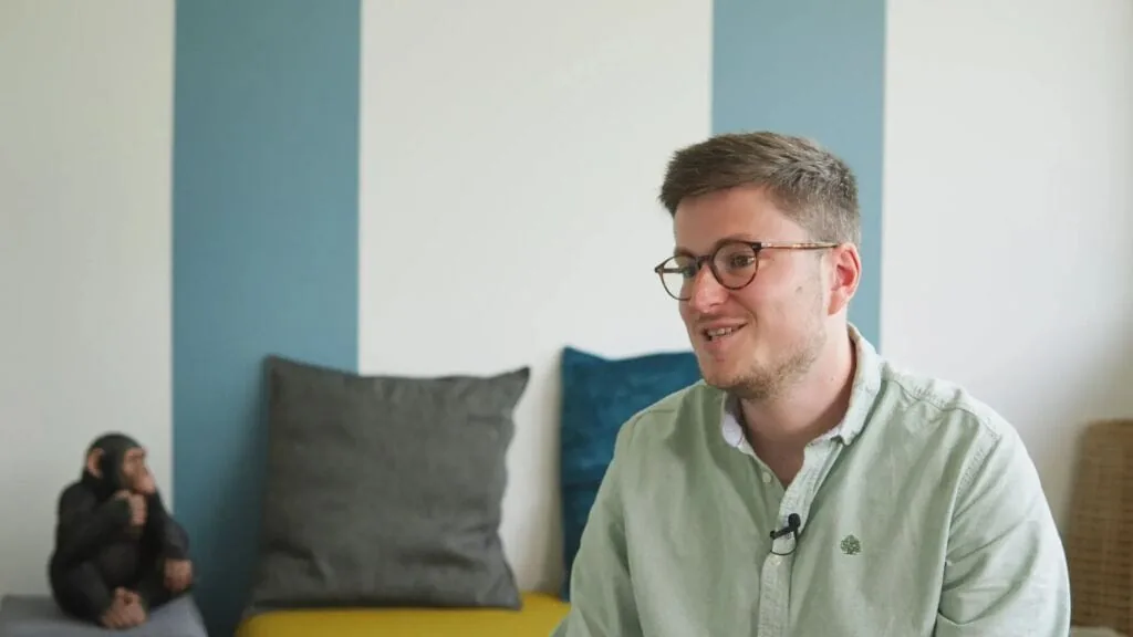 Man in glasses and light green shirt with a chimpanzee statue in the background.