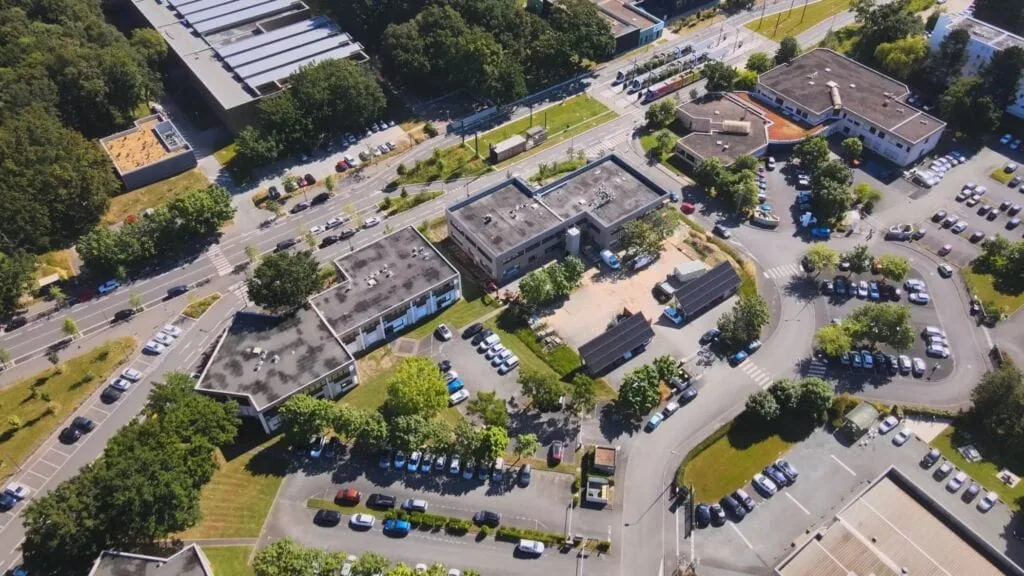 Aerial view of buildings, parking lots, and green spaces in an urban area.