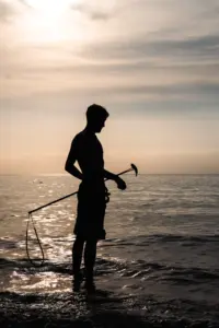 Silhouette of a person standing in shallow water at sunset, holding a paddle and a paddleboard leash—a serene moment captured by Embodic Films.