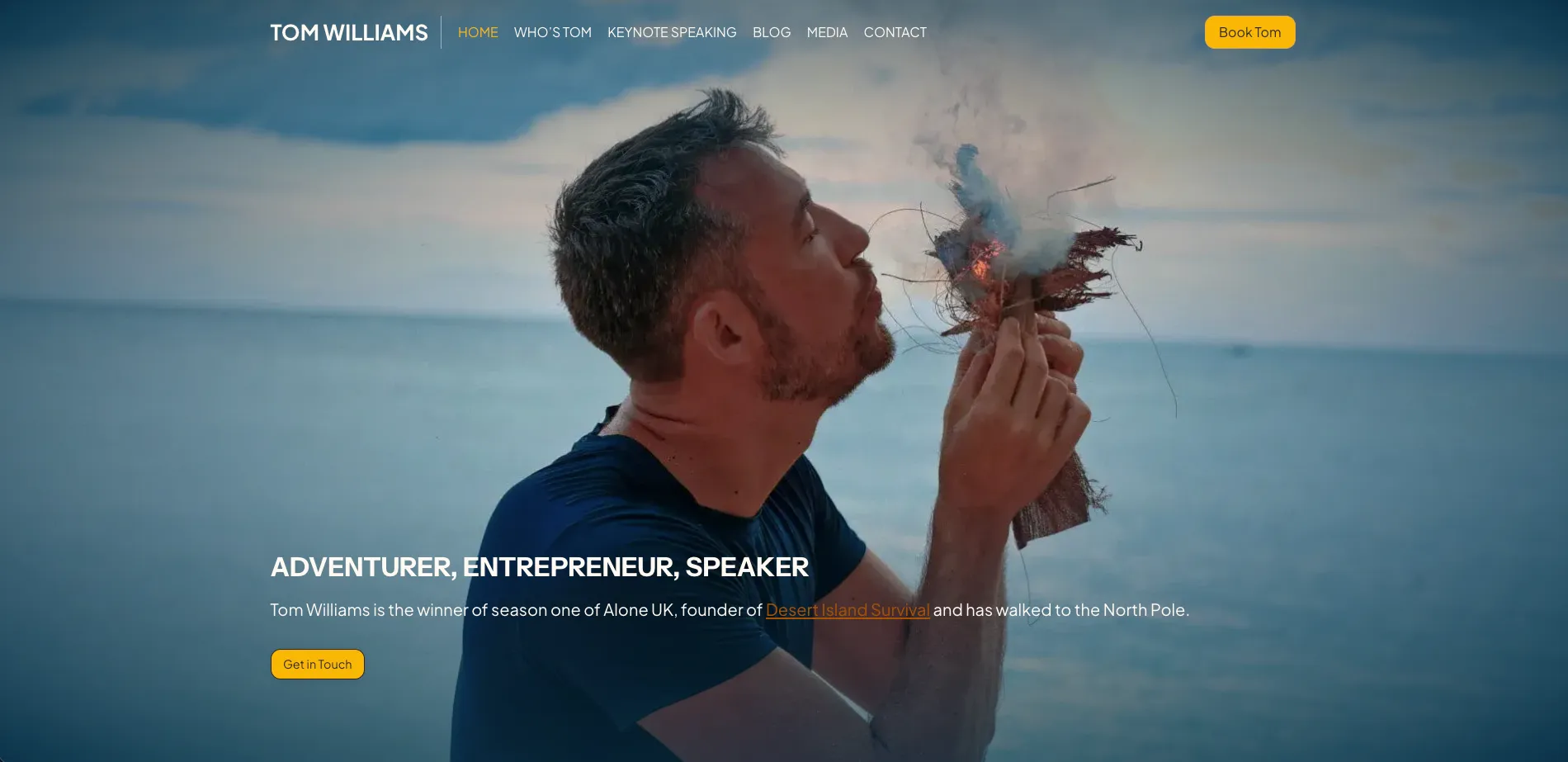 Tom Williams, adventurer and speaker, blowing on a small fire near the sea.