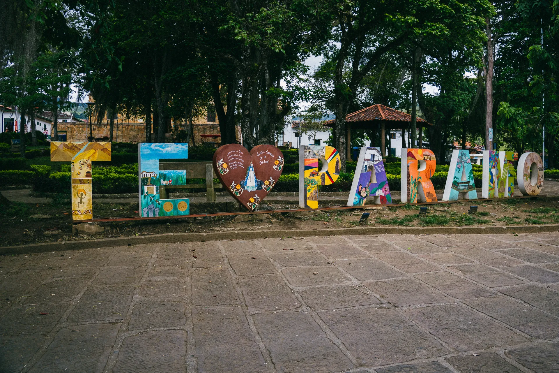 Colorful "El Páramo" sign in park, trees and buildings in background.