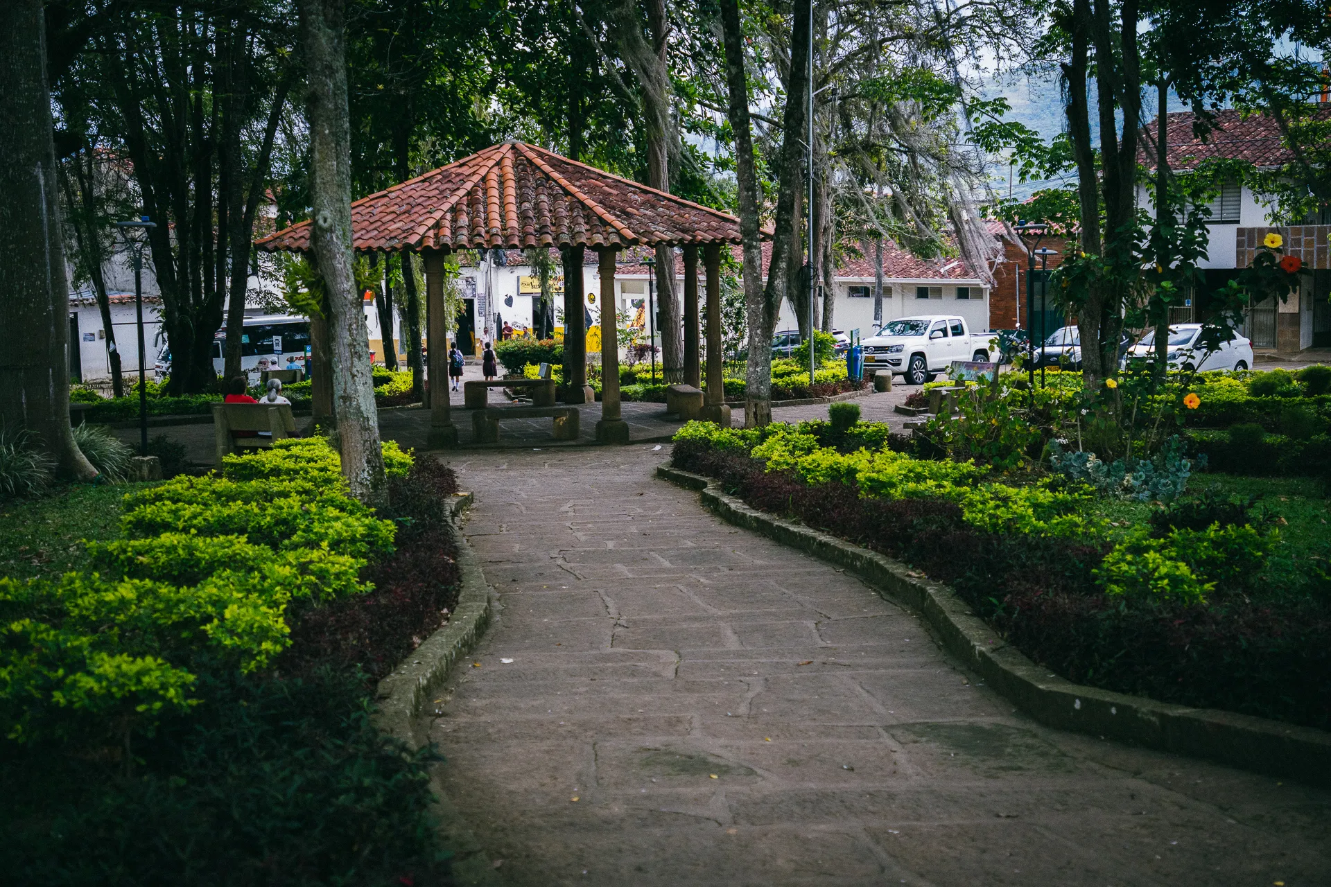 Park path leading to gazebo in El Páramo, Colombia. Lush green foliage and trees surround the walkway.