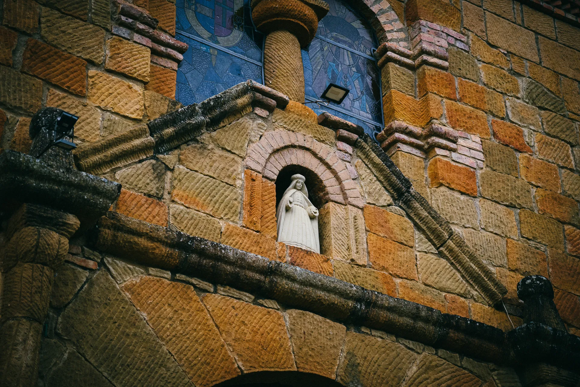 Stone church facade with Virgin Mary statue and stained glass window.